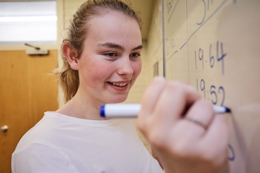 student writing down answers on a whiteboard