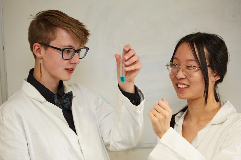student looking at a test tube with blue liquid inside, as another student looks on