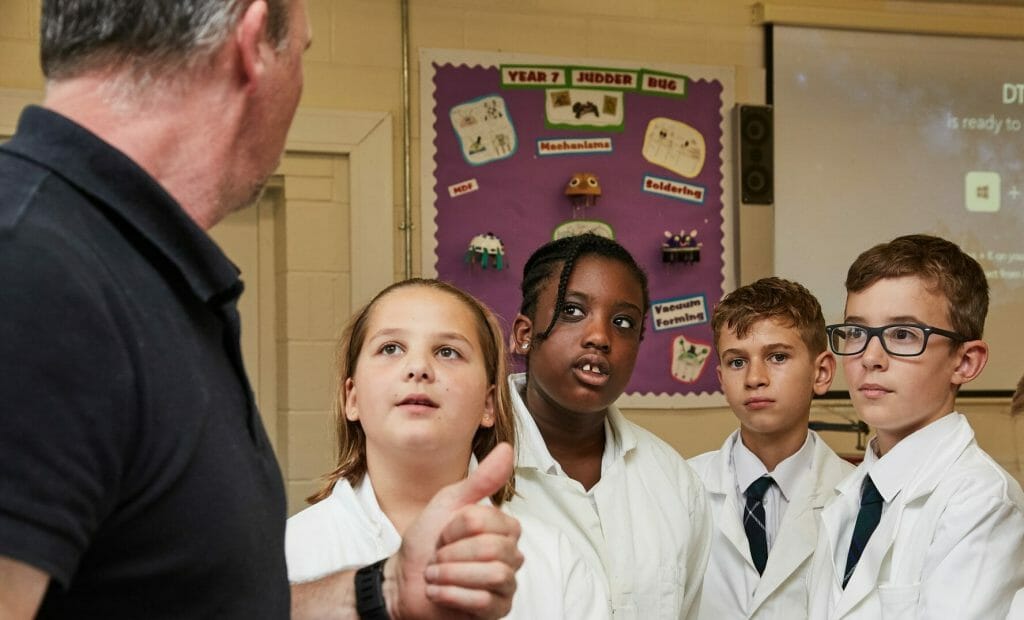 children in lab coats listening to their teacher