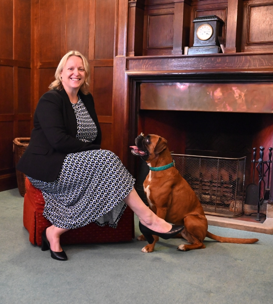 Claire Gilding-Brant, Interim Head of Luckley House School, sitting in front of a fireplace with a dog at her feet, smiling warmly.